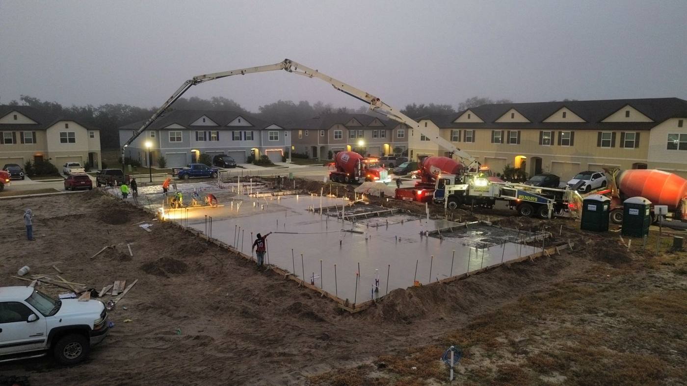 WDB boom pouring a slab in a townhome community at dawn with three mixer trucks